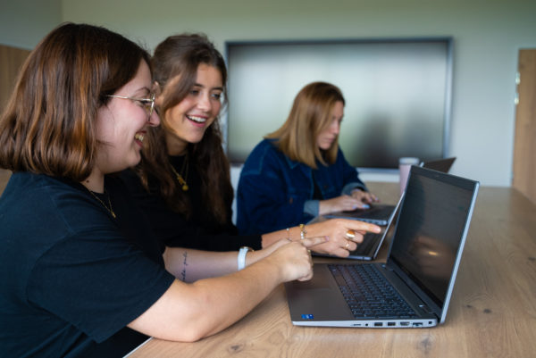 Trois femmes font des recherches sur leurs ordinateurs pour construire la stratégie de marque employeur d'un client We Feel Good