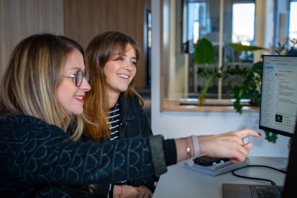 Deux collaboratrices devant un écran d'ordinateur dans les bureaux de l'agence We Feel Good