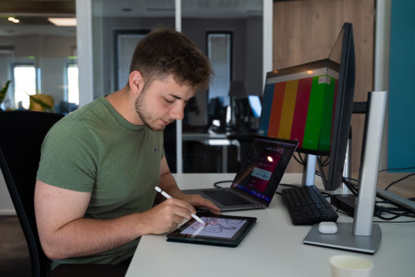 Un collaborateur spécialisé en graphisme et en design utilise son ordinateur et une tablette graphique dans les bureaux de l'agence We Feel Good