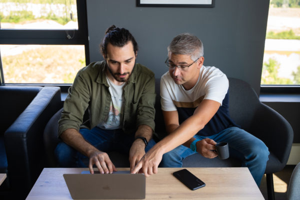 Deux collaborateurs assis dans un canapé devant un ordinateur en réunion pour préparer un projet client We Feel Good